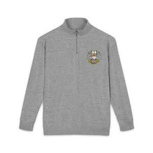 May include: A heather gray long-sleeve pullover with a quarter-zip neckline. The sweatshirt features a crest design on the chest with a winged emblem and banner in yellow, white, and black. The garment is made of a soft, comfortable material.