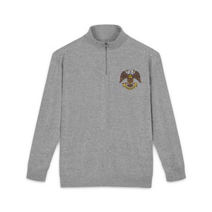 May include: A gray long-sleeve sweatshirt with a quarter-zip collar. The sweatshirt features a colorful embroidered emblem of an eagle with a banner. The emblem is in shades of gold, brown, and yellow.
