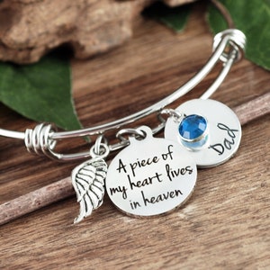 May include: A silver charm bracelet with a blue crystal charm, a wing charm, and two round charms with the text "A piece of my heart lives in heaven" and "Dad".