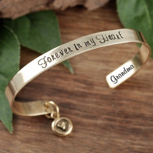 Puede incluir: Pulsera dorada con un dije en forma de coraz&oacute;n. La pulsera est&aacute; grabada con las palabras "Forever in my Heart" y "Grandma".
