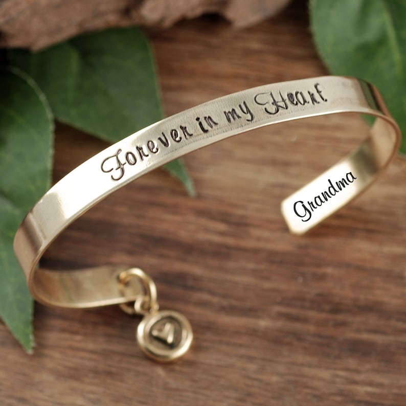 Puede incluir: Pulsera dorada con un dije en forma de coraz&oacute;n. La pulsera est&aacute; grabada con las palabras "Forever in my Heart" y "Grandma".