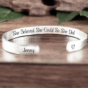 May include: Silver cuff bracelet with the inscription "She Believed She Could So She Did" and the name "Jenny" engraved on the inside. A small heart is engraved on the other side.