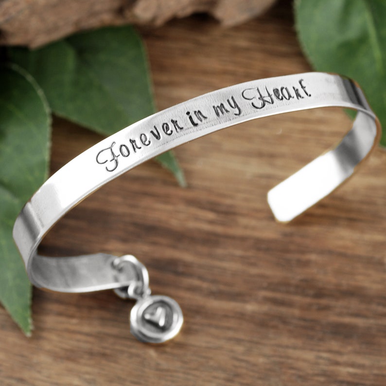 Puede incluir: Pulsera de plata con un dije que dice "Forever in my Heart".