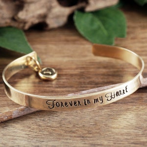 Puede incluir: Pulsera de brazalete de oro con un dije y la inscripci&oacute;n "Forever in my heart".