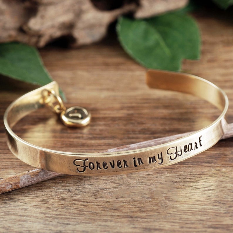 Puede incluir: Pulsera de brazalete de oro con un dije y la inscripci&oacute;n "Forever in my heart".
