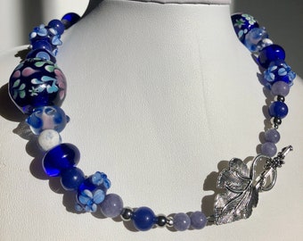 16+1/2" Choker made with stainless steel, lapis lazuli, torch fired beads. Cobalt blue and lavender tones. Metal leaf clasp