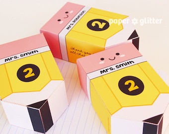 May include: Three pink and yellow pencil-shaped boxes with a smiling face and the number 2 on each. The boxes are labeled "Mrs. Smith" and "Mrs. Robinson". The text "Thank you for all that you do" is on one of the boxes. The text "paper & glitter" is in the top right corner of the image.