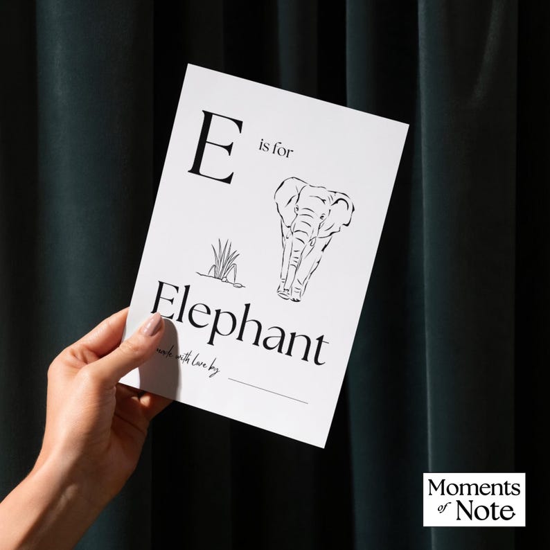May include: A white card with the letter "E" and the words "is for Elephant" in a stylish font. The card features a black and white illustration of an elephant and grass. The words "made with love by" are at the bottom.