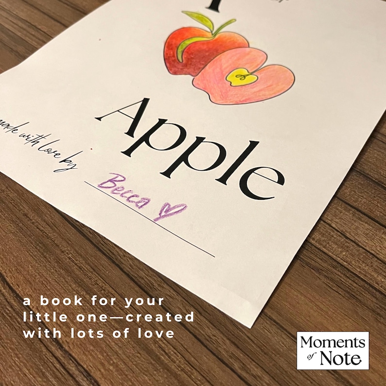 May include: A hand-drawn illustration of an apple with the word "Apple" in large black letters. The text "made with love by Becca" and "a book for your little one - created with lots of love" are also present. The image is on a wooden surface.