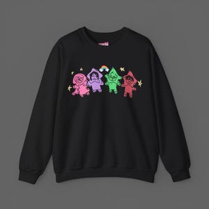 May include: Black crewneck sweatshirt featuring a colorful graphic of four cartoon figures in pink, purple, green, and red, each with a star-shaped head. A rainbow and stars are above the figures. The word "manchi" is printed on the top.