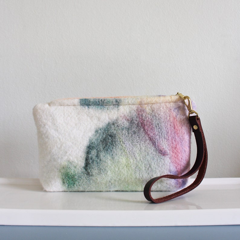 May include: A white clutch bag with a colorful abstract design and a brown leather strap.