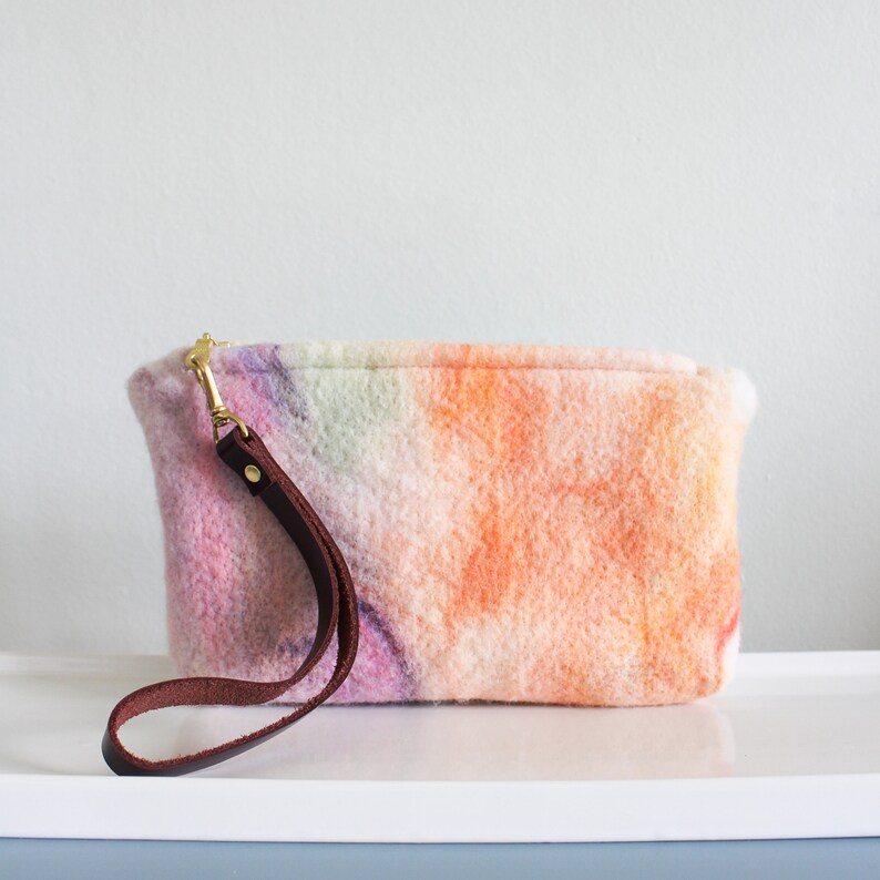 May include: A small, pink, orange, and green tie-dye clutch bag with a brown leather strap.
