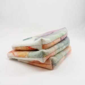 May include: Three colorful felted fabric pouches stacked on top of each other. The pouches are made of a soft, textured fabric and have a variety of colors, including white, orange, yellow, green, and purple.
