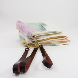 May include: Three colorful fabric pouches with gold zippers and brown leather straps. The pouches are stacked on top of each other and the straps are hanging down.