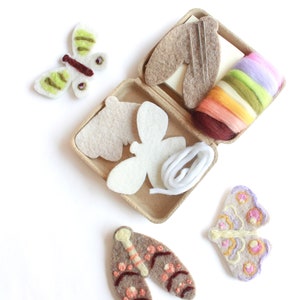 May include: A craft kit for making felt butterflies. The kit includes two white felt butterfly shapes, a skein of colorful embroidery floss, a small spool of white thread, two needles, and a brown felt butterfly with embroidery details.
