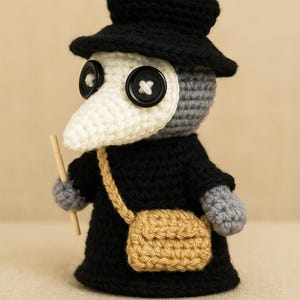 Puede incluir: Muñeca de ganchillo hecha a mano de un médico de la peste, con sombrero y abrigo negros, una máscara blanca en forma de pico y una pequeña bolsa de color canela. La muñeca tiene grandes ojos de botón y sostiene un palito de madera.