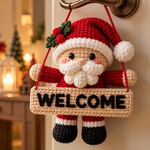 May include: A crocheted Santa Claus hanging decoration featuring a red hat with a white pom-pom, a white beard, and black boots. The figure holds a rectangular beige sign with the black text WELCOME, suspended by a red cord from a door handle.