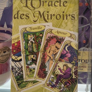 Peut inclure: Une boîte jaune avec le titre "L'Oracle des Miroirs" et une illustration colorée de quatre cartes de tarot. Les cartes représentent des thèmes de famille, d'amour, de voyage et de l'inconnu. La boîte comprend également le nom "Dimitri d'Alfange d'Uvril®".