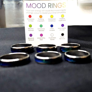May include: Six mood rings with colour-changing properties, each showing a different shade. A card explains how the rings change colour to reflect emotions. The rings have a silver band and a dark, colour-shifting centre.