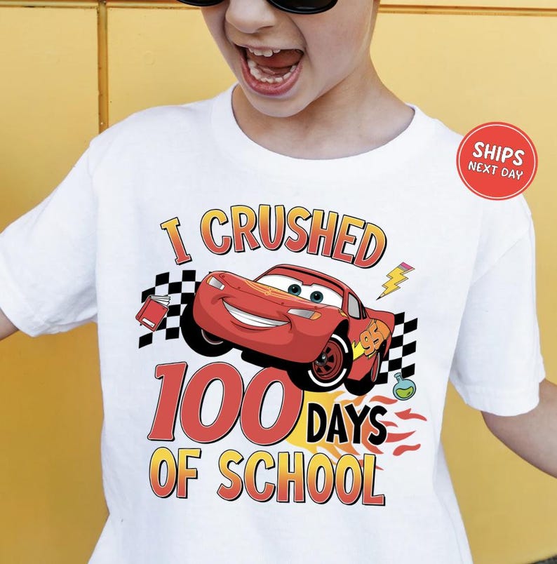 A person wearing a white t-shirt with a graphic design featuring a red car and the text "I CRUSHED 100 DAYS OF SCHOOL".