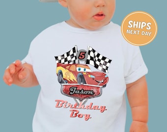 May include: White t-shirt featuring a red cartoon race car with the number 95, checkered flags, and the text "Jason Birthday Boy". The number 5 is above the car. The shirt is for a child.