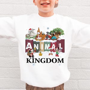 A white sweatshirt with a colorful graphic design featuring various Disney characters and the text "ANIMAL KINGDOM".