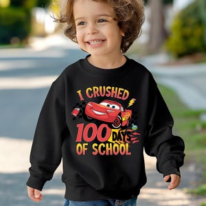 a young boy wearing a black sweatshirt with cars printed on it