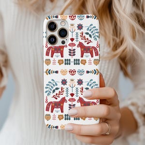 May include: A white iPhone case with a colorful Scandinavian folk art design featuring red, blue, and yellow horses and flowers.