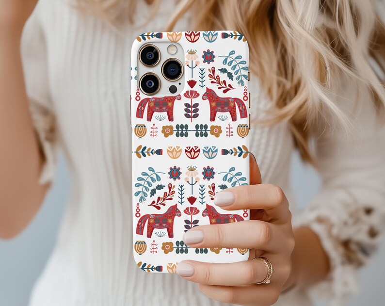 May include: A white iPhone case with a colorful Scandinavian folk art design featuring red, blue, and yellow horses and flowers.