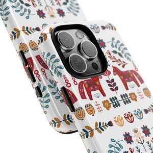 May include: White iPhone case with a colorful Scandinavian folk art design featuring red and white horses, flowers, and leaves.