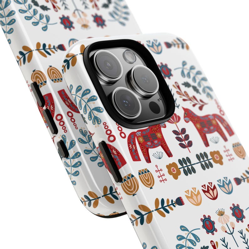 May include: White iPhone case with a colorful Scandinavian folk art design featuring red and white horses, flowers, and leaves.