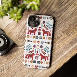May include: A white phone case with a colorful Scandinavian folk art design featuring red horses, flowers, and leaves.