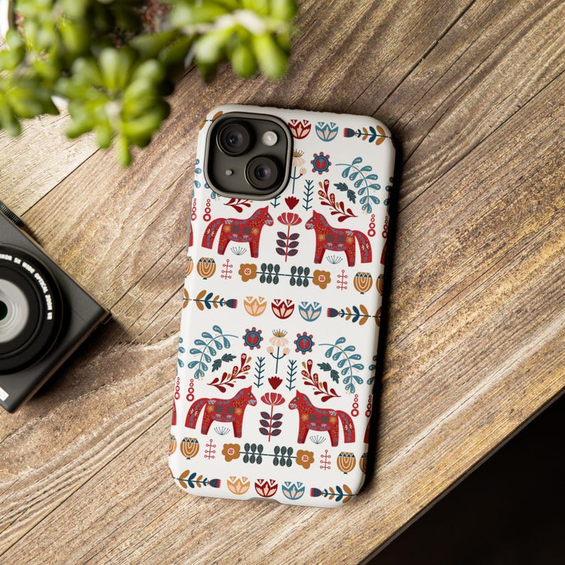 May include: A white phone case with a colorful Scandinavian folk art design featuring red horses, flowers, and leaves.