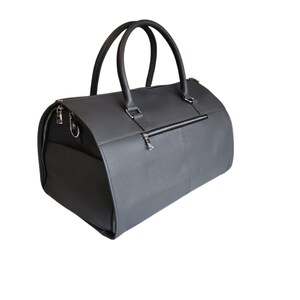 May include: A gray duffel bag with two rounded handles and a zippered closure. The bag has a rectangular shape with a side pocket and a zipper on the back. The bag is made of a textured material.