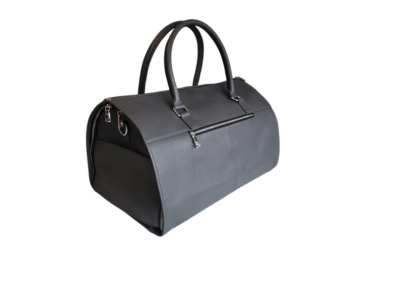 May include: A gray duffel bag with two rounded handles and a zippered closure. The bag has a rectangular shape with a side pocket and a zipper on the back. The bag is made of a textured material.