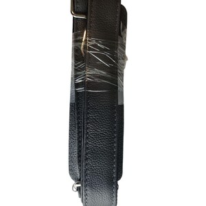 May include: A black, textured leather bag strap with silver-colored metal hardware. The strap is wrapped in clear plastic. The strap is designed to be adjustable and is likely for a shoulder bag or purse.