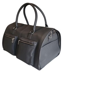 May include: A dark gray leather duffel bag with two front pockets with zippers and a side pocket. The bag has two top handles and silver-tone hardware. The bag is designed for travel and has a rounded shape.