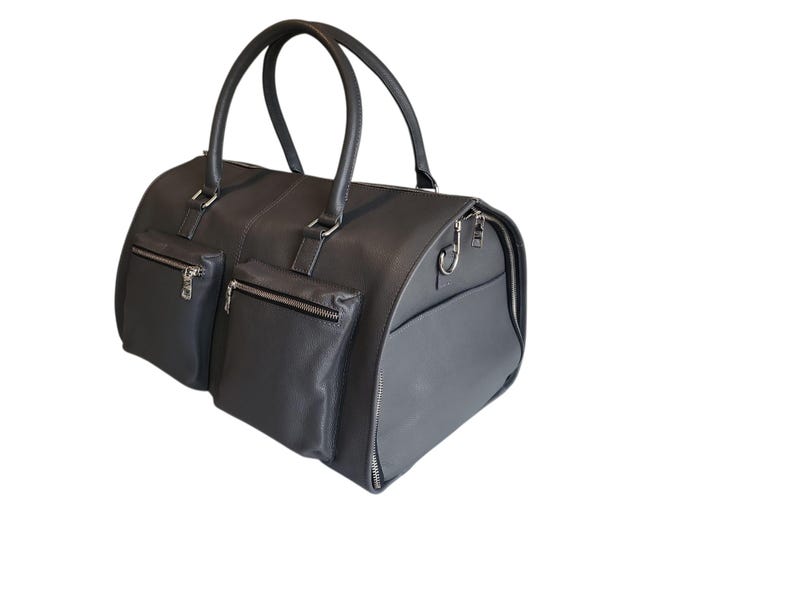 May include: A dark gray leather duffel bag with two front pockets with zippers and a side pocket. The bag has two top handles and silver-tone hardware. The bag is designed for travel and has a rounded shape.