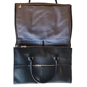 May include: Black leather garment bag with a top handle and two smaller handles. The bag has a zippered compartment on the top and a larger compartment below. The interior is lined with gray fabric.