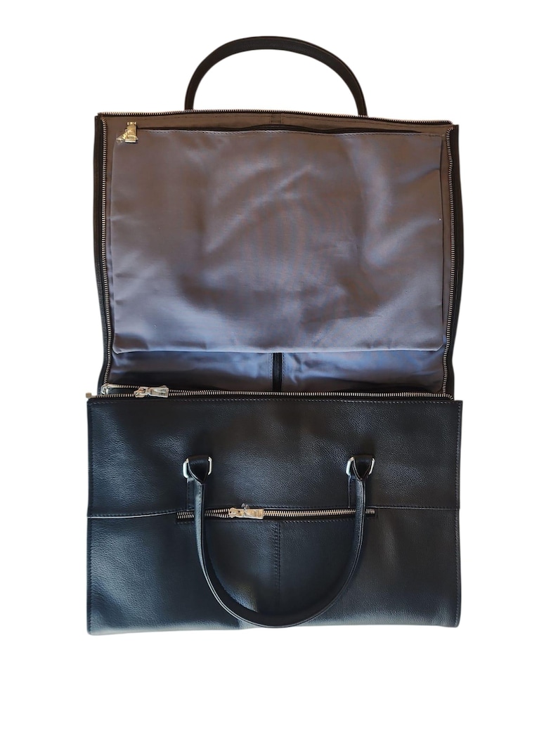 May include: Black leather garment bag with a top handle and two smaller handles. The bag has a zippered compartment on the top and a larger compartment below. The interior is lined with gray fabric.