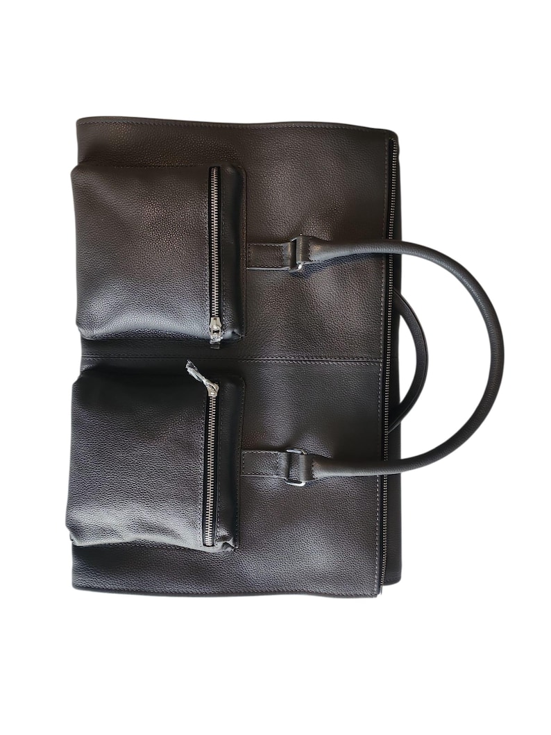 May include: Dark brown leather briefcase with two zippered pockets on the front. The briefcase has a handle and a buckle closure. The bag is made of a textured leather material.
