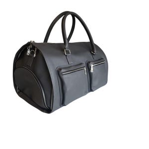 May include: A dark gray duffel bag with two exterior zippered pockets and a zippered side pocket. The bag has two top handles and a detachable shoulder strap. The hardware is silver-toned.