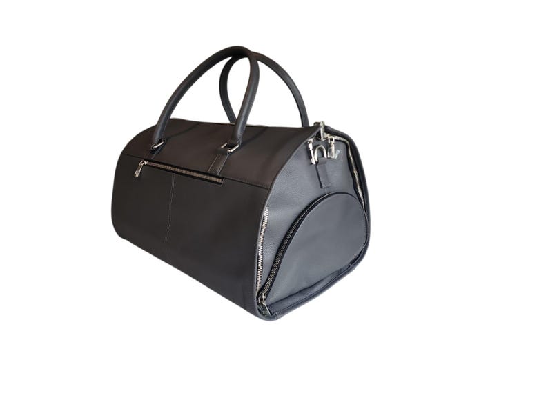 May include: A black duffel bag with a rounded shape, featuring two top handles and a side pocket. The bag has a zipper closure and silver-colored hardware. The material appears to be leather or a leather-like material.