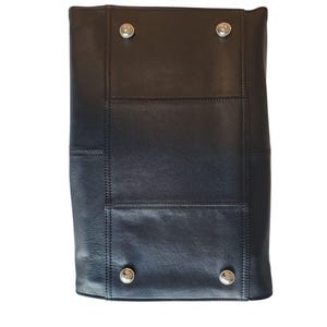 May include: Black leather tote bag with silver-tone metal studs. The bag has a rectangular shape with stitched panels and a structured design. The studs are placed at the corners of the bag. The bag is made of a smooth, matte leather.