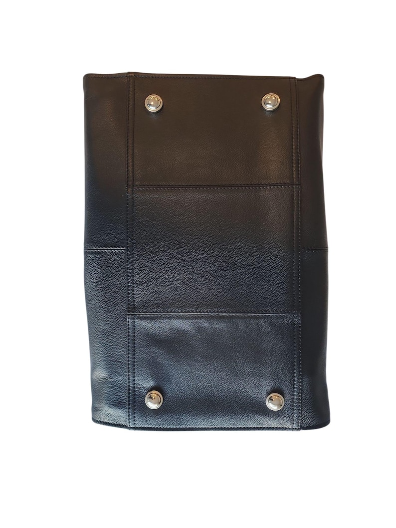 May include: Black leather tote bag with silver-tone metal studs. The bag has a rectangular shape with stitched panels and a structured design. The studs are placed at the corners of the bag. The bag is made of a smooth, matte leather.