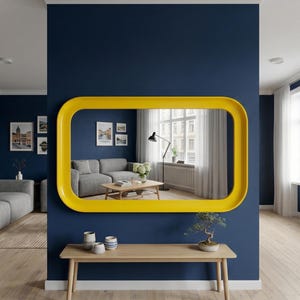 May include: A large, horizontal, rectangular wall mirror with a thick, smooth, bright yellow frame. The mirror is mounted on a dark blue wall above a light-colored wooden bench, reflecting a room with a gray sofa and a wooden coffee table.