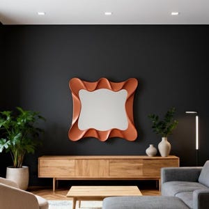 May include: A modern living room featuring a large, wavy-edged mirror with a copper-colored frame. Below the mirror is a wooden cabinet. The room includes a gray sectional sofa, a beige armchair, and a potted plant, creating a stylish interior design.