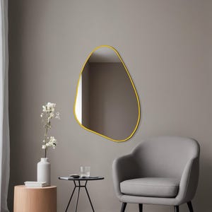 May include: An irregular, pebble-shaped wall mirror featuring a thin, vibrant yellow frame. The mirror has a smooth, organic outline that contrasts with the surrounding space, reflecting the interior environment within its reflective glass surface.
