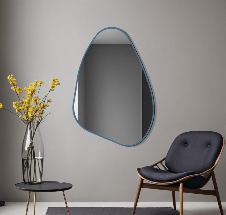 May include: An irregular, pebble-shaped wall mirror with a thin, matte blue frame. The mirror features a smooth, organic outline that deviates from traditional geometric shapes, providing a reflective surface with a distinct, asymmetrical contour.