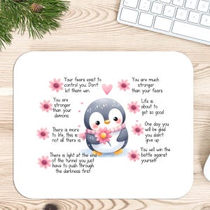 May include: A white mousepad featuring a cute cartoon penguin with a pink scarf and flower. The mousepad has inspirational text and pink flower accents. A computer keyboard and mouse are in the background.